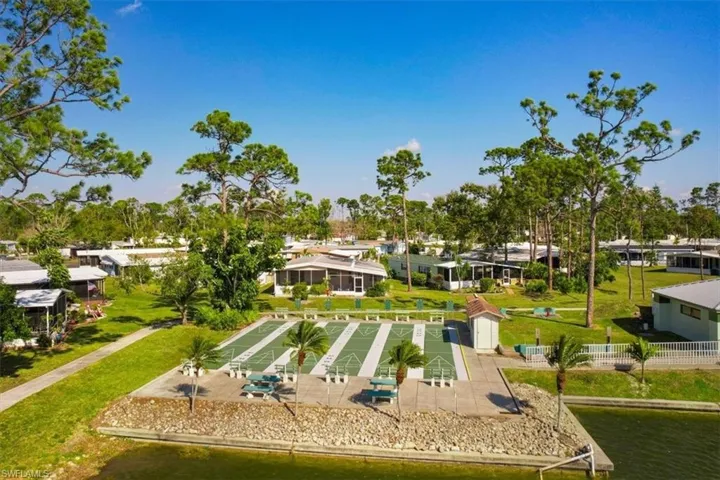 Waterfront property featuring multiple shuffleboard courts, mature palm trees, and a manicured green space