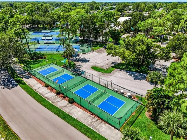 Multiple pickleball courts with blue playing surfaces, several tennis courts, and ample paved parking, all surrounded by mature landscaping
