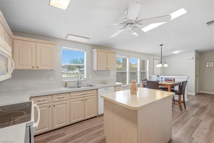 Kitchen featuring wood-finish flooring, light-toned cabinetry, a kitchen island, and a dining area with pendant lighting
