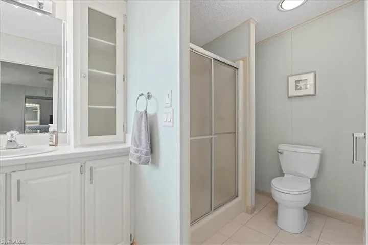White vanity with an integrated sink, white cabinetry with frosted glass inserts, and a walk-in shower with sliding glass doors