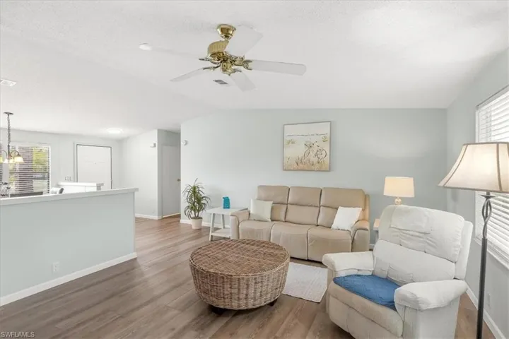 Wood-finish flooring throughout, ceiling fan with brass accents, light blue wall paint, white window blinds, and white trim