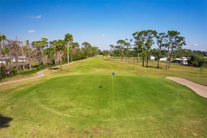 Expansive golf course green with a flagstick, bordered by a paved cart path and mature trees