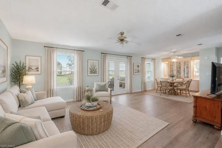 Spacious living area featuring wood-finish flooring, abundant natural light from multiple windows, and a ceiling fan