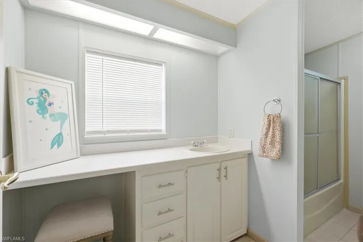 White vanity with an integrated sink, built-in cabinetry, and window with blinds