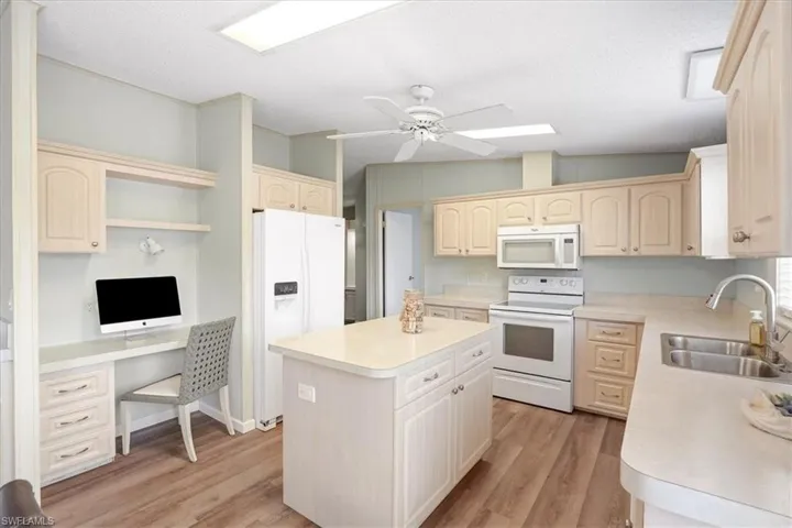 Kitchen with wood-finish flooring, light-toned cabinetry, a central island, and white appliances