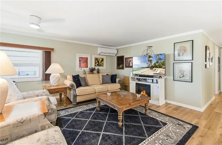 Living room featuring crown molding, wood finished floors, a wall unit AC, and a warm lit fireplace