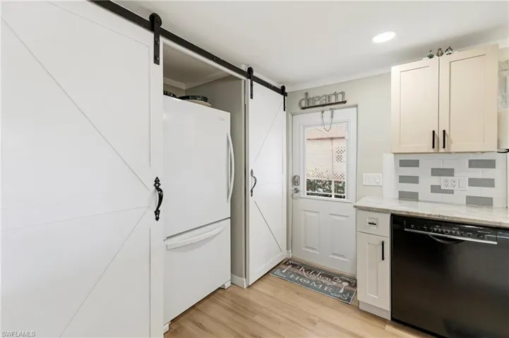 Kitchen with black dishwasher, freestanding refrigerator, white cabinetry, light wood-style floors, and recessed lighting