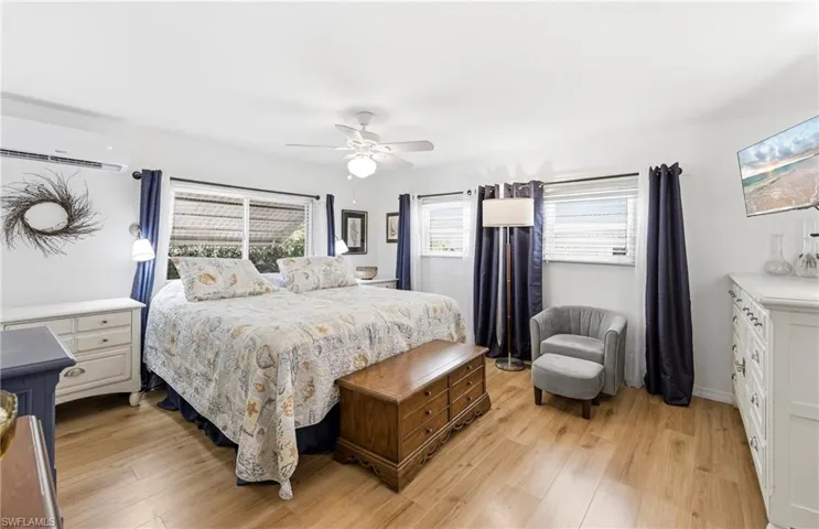 Bedroom with a wall unit AC, light wood-type flooring, a ceiling fan, and multiple windows
