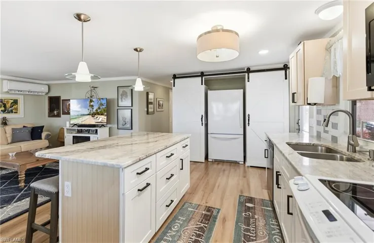 Kitchen with a barn door, light stone counters, white appliances, pendant lighting, and a kitchen breakfast bar
