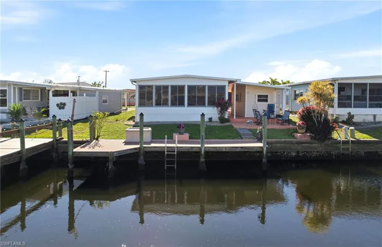 Back of property with a water view, a sunroom, a patio, and a lawn