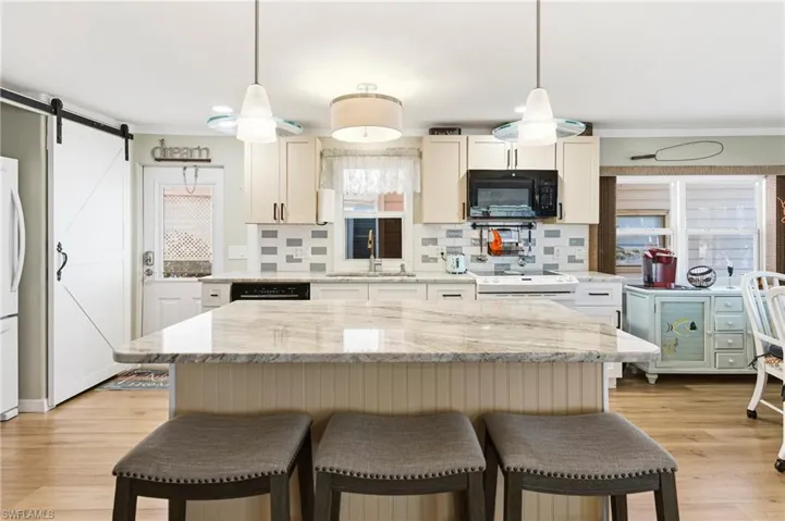 Kitchen with a breakfast bar area, backsplash, a center island, black appliances, and pendant lighting