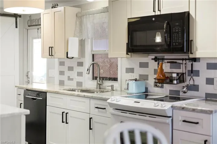 Kitchen featuring black appliances, backsplash, light stone counters, and white cabinets