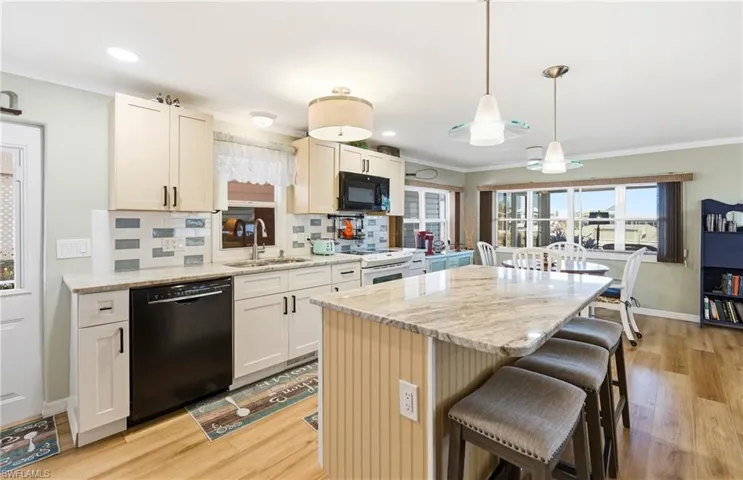 Kitchen with black appliances, light stone countertops, tasteful backsplash, a center island, and decorative light fixtures