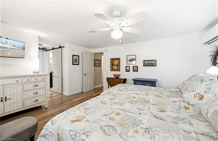 Bedroom with a barn door, ceiling fan, light wood-type flooring, and a wall unit AC