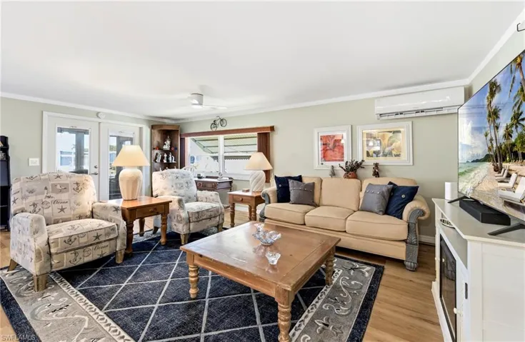 Living area with light wood finished floors, crown molding, a wall mounted air conditioner, french doors, and ceiling fan