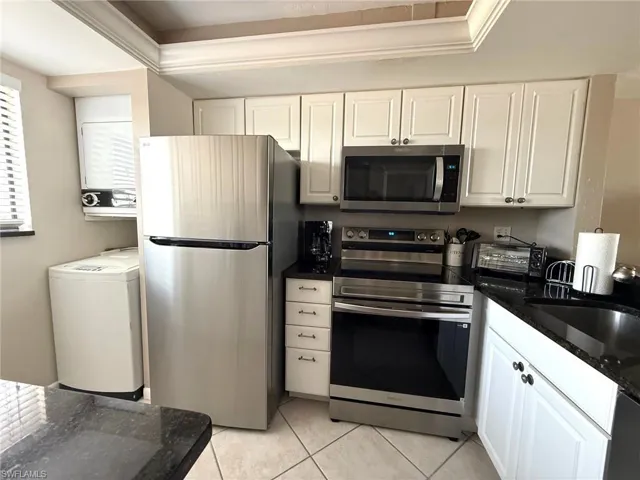 Kitchen featuring stainless steel appliances, white cabinets, washer / dryer, dark stone counters, and light tile patterned flooring