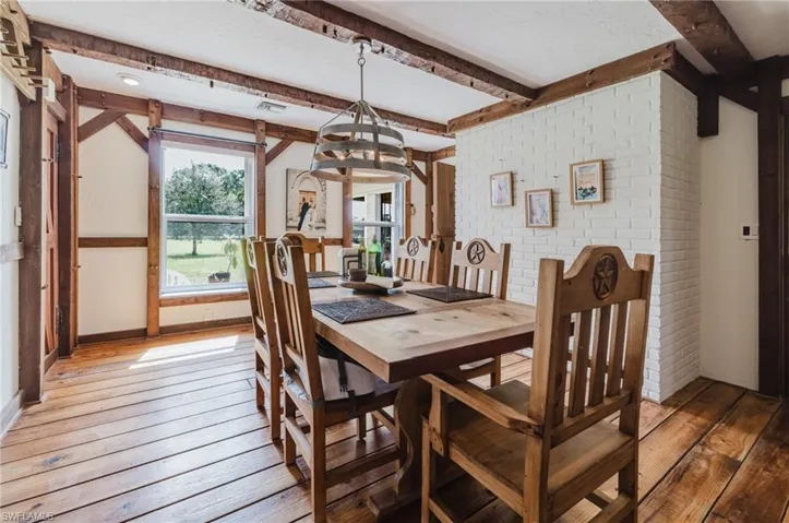 Exposed wood beam ceiling, wood-finish flooring, white brick accent wall, and a window framing outdoor scenery