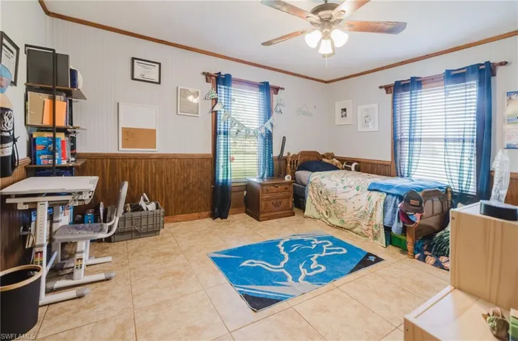 Neutral-toned tile flooring, wood paneling, paneled walls, and a ceiling fan with integrated lighting