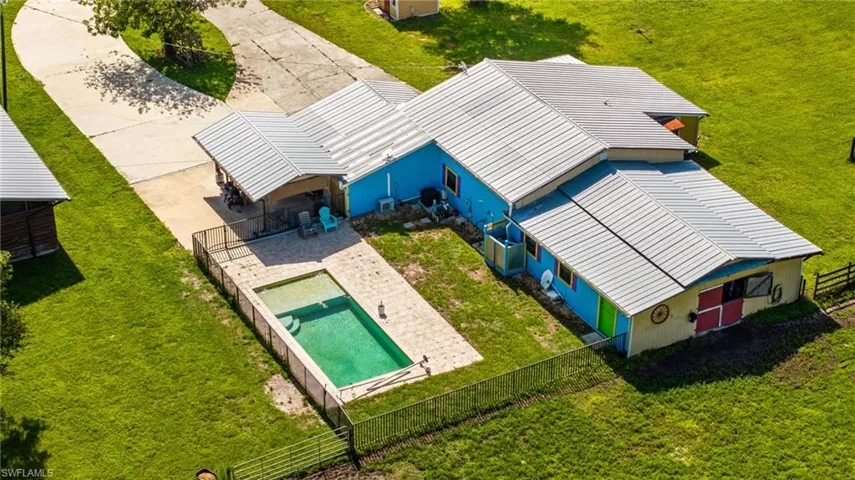 Expansive property featuring a vibrant main structure, a metal roof, an in-ground swimming pool with surrounding hardscaping, a fenced pool area, and a paved driveway
