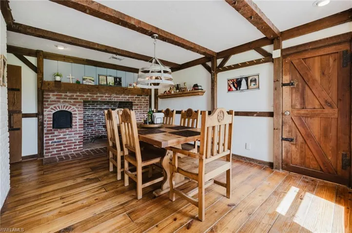 Wood-finish flooring with exposed ceiling beams, a brick fireplace, and a wood plank door with black hardware