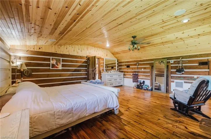 Wood-finish flooring, wood-paneled walls, vaulted wood-paneled ceiling, and a ceiling fan with light fixture