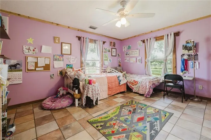 Room featuring a ceiling fan, two windows with blinds and drapes, and tile flooring