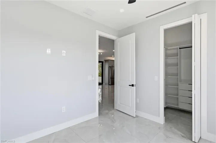 Unfurnished bedroom featuring freestanding refrigerator, light marble finish flooring, a walk in closet, recessed lighting, and a ceiling fan