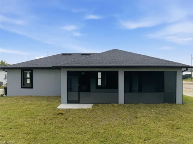 Rear view of house with a shingled roof, a sunroom, a lawn, and stucco siding