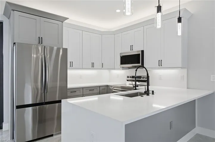 Kitchen featuring stainless steel appliances, a peninsula, hanging light fixtures, light stone counters, and white cabinetry