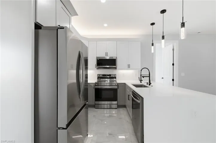 Kitchen with stainless steel appliances, a peninsula, light stone countertops, pendant lighting, and light marble finish floors