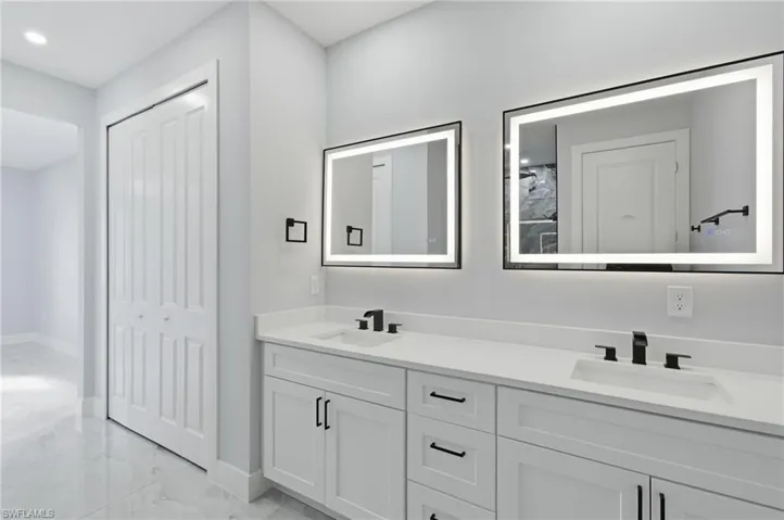 Bathroom with double vanity, light marble finish floors, and recessed lighting