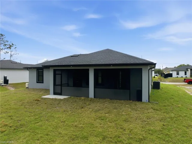 Back of property featuring a lawn, roof with shingles, stucco siding, and a sunroom