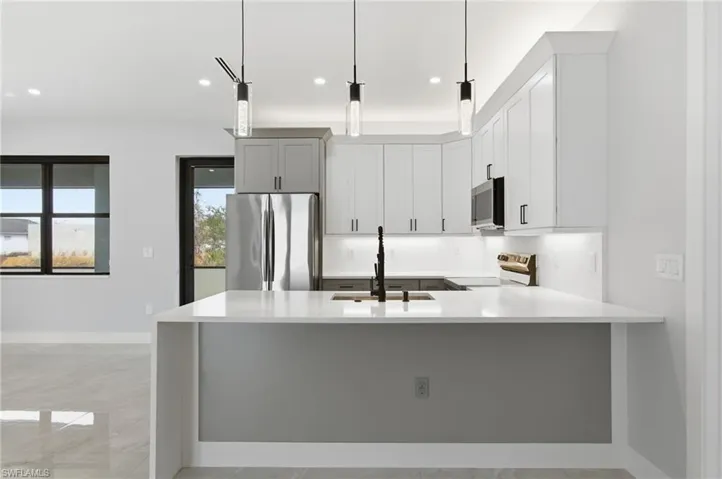 Kitchen featuring a peninsula, light stone countertops, stainless steel appliances, decorative light fixtures, and white cabinets
