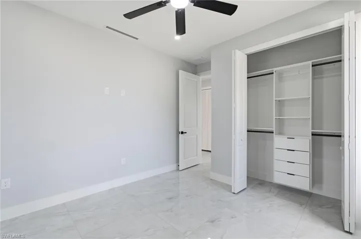 Unfurnished bedroom with ceiling fan, light marble finish floors, and a closet