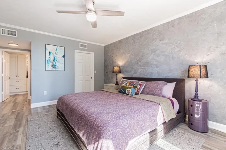 Bedroom featuring ornamental molding, light wood-style vinyl floors, ceiling fan, wallpapered walls, and an accent wall