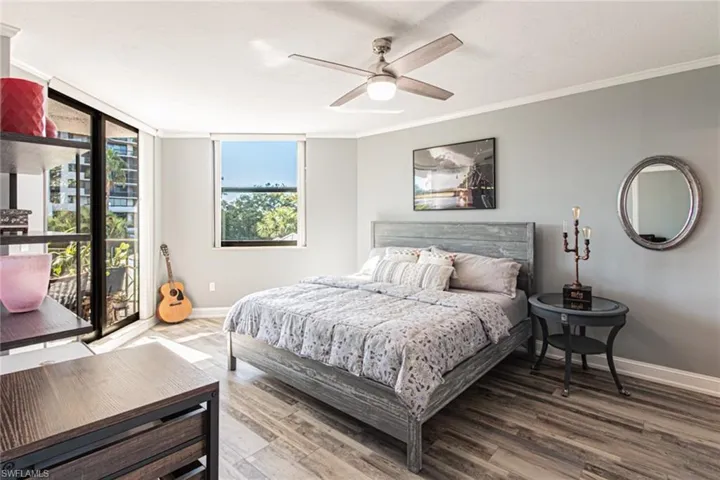 Bedroom with wood finished floors, ornamental molding, a ceiling fan, and a wall of windows