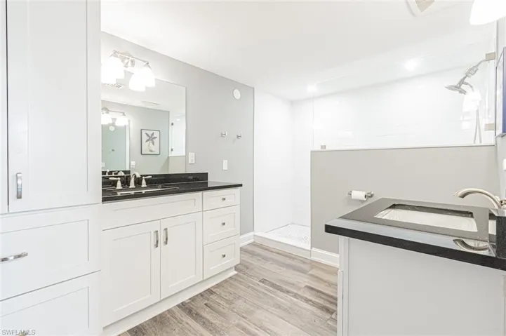 Full bath with two vanities, walk in shower, and light vinyl flooring.