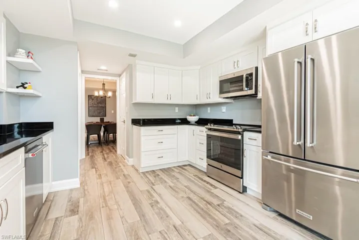 Kitchen featuring appliances with stainless steel finishes, white cabinets, a chandelier, light wood vinyl floors, and open shelves