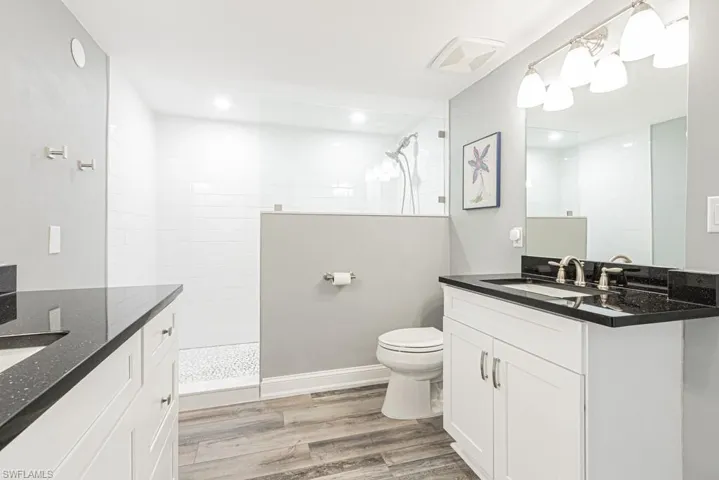 Bathroom with two vanities, a walk in shower, light wood-style floors, and recessed lighting