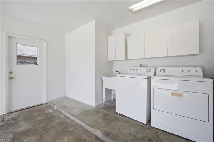 Dedicated laundry area featuring a utility sink, white upper cabinetry, and a service door with a window