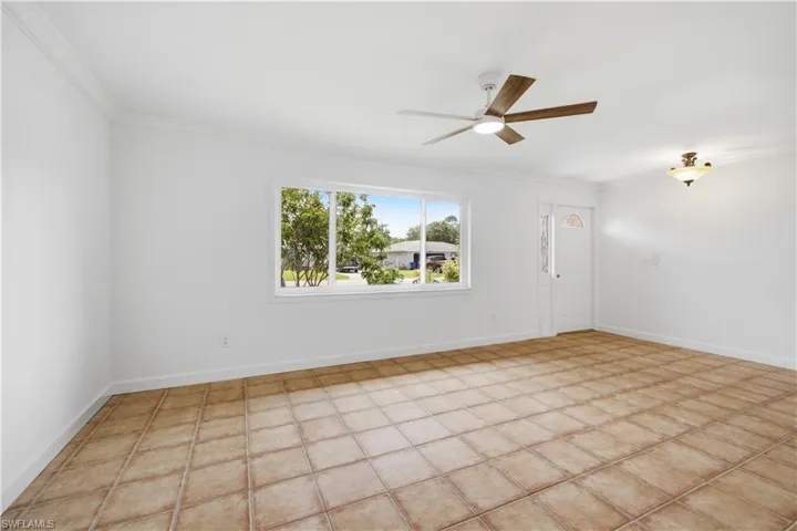 Spacious interior featuring large windows, neutral tile flooring, crown molding, a contemporary ceiling fan, and a decorative light fixture