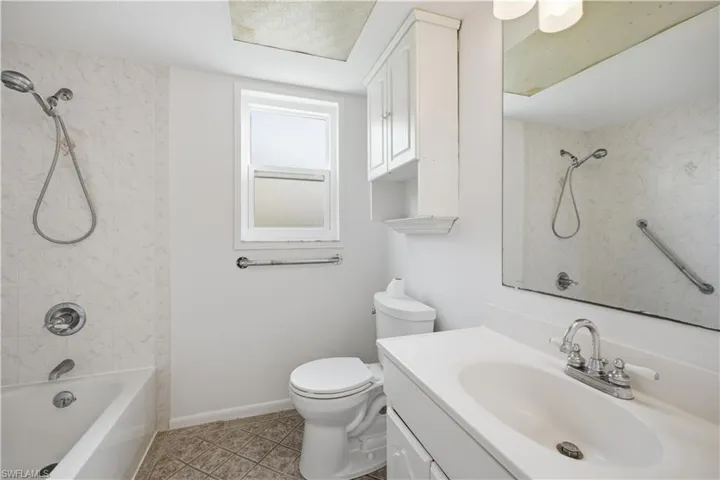 Full bathroom featuring a white vanity with integrated sink, chrome fixtures, a combination tub and shower with white tile surround, and a white framed window