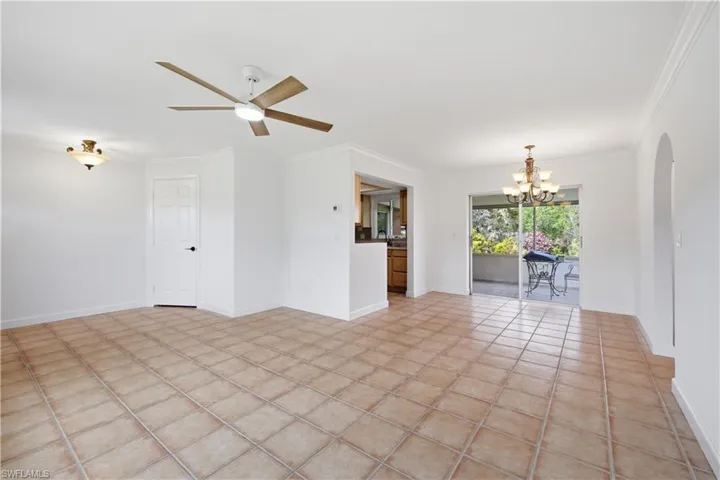 Spacious open-concept room featuring warm-toned tile flooring, white walls, and crown molding