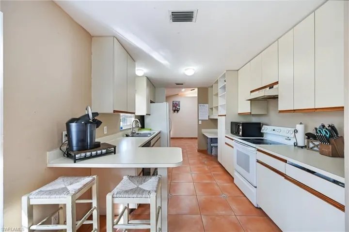 Dual tone kitchen with light countertops, white appliances, light tile patterned flooring, two tone cabinetry, and a breakfast bar
