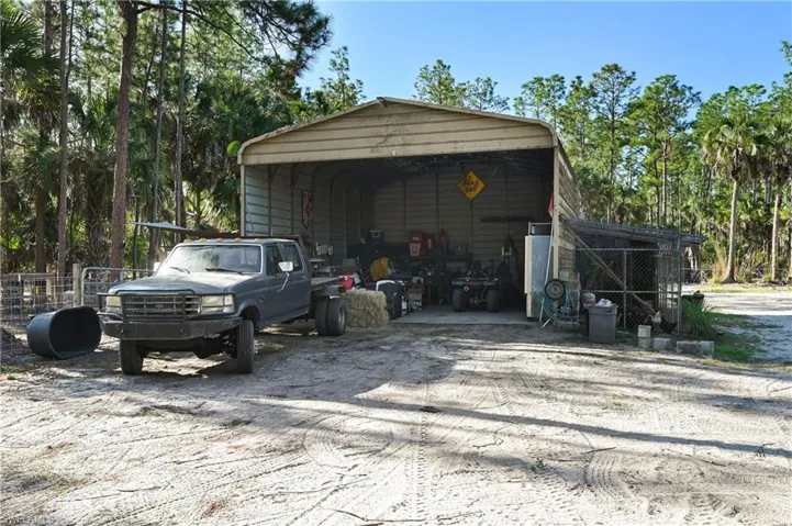 Garage featuring a carport, dirt driveway, and view of scattered trees