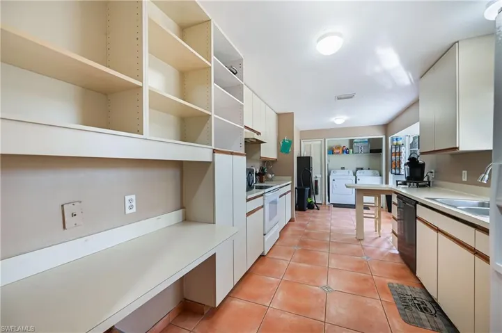 Dual tone kitchen with light countertops, separate washer and dryer, light tile patterned floors, white range with electric cooktop, and two tone color scheme