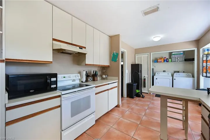 Dual tone kitchen with white electric range oven, light countertops, black microwave, washer and dryer, and dual tone cabinetry