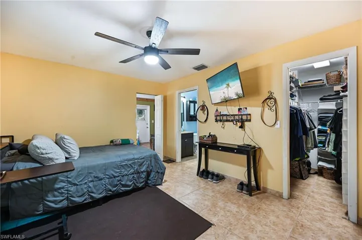 Bedroom featuring light tile patterned floors, a walk in closet, a ceiling fan, and ensuite bath
