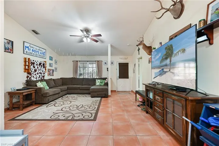 Living room featuring lofted ceiling, a ceiling fan, and light tile patterned floors