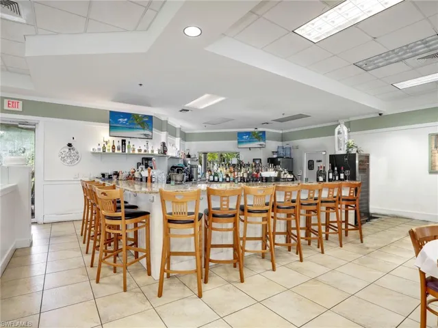 Bar with light stone counters, stainless steel fridge, white cabinets, and light tile patterned flooring